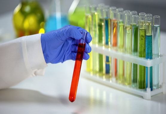 Gloved hand holding a tube of dye next to a rack of dye-filled tubes.