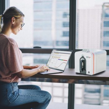 Woman seated at a table working on a laptop next to a Datacolor Spectro 1000.